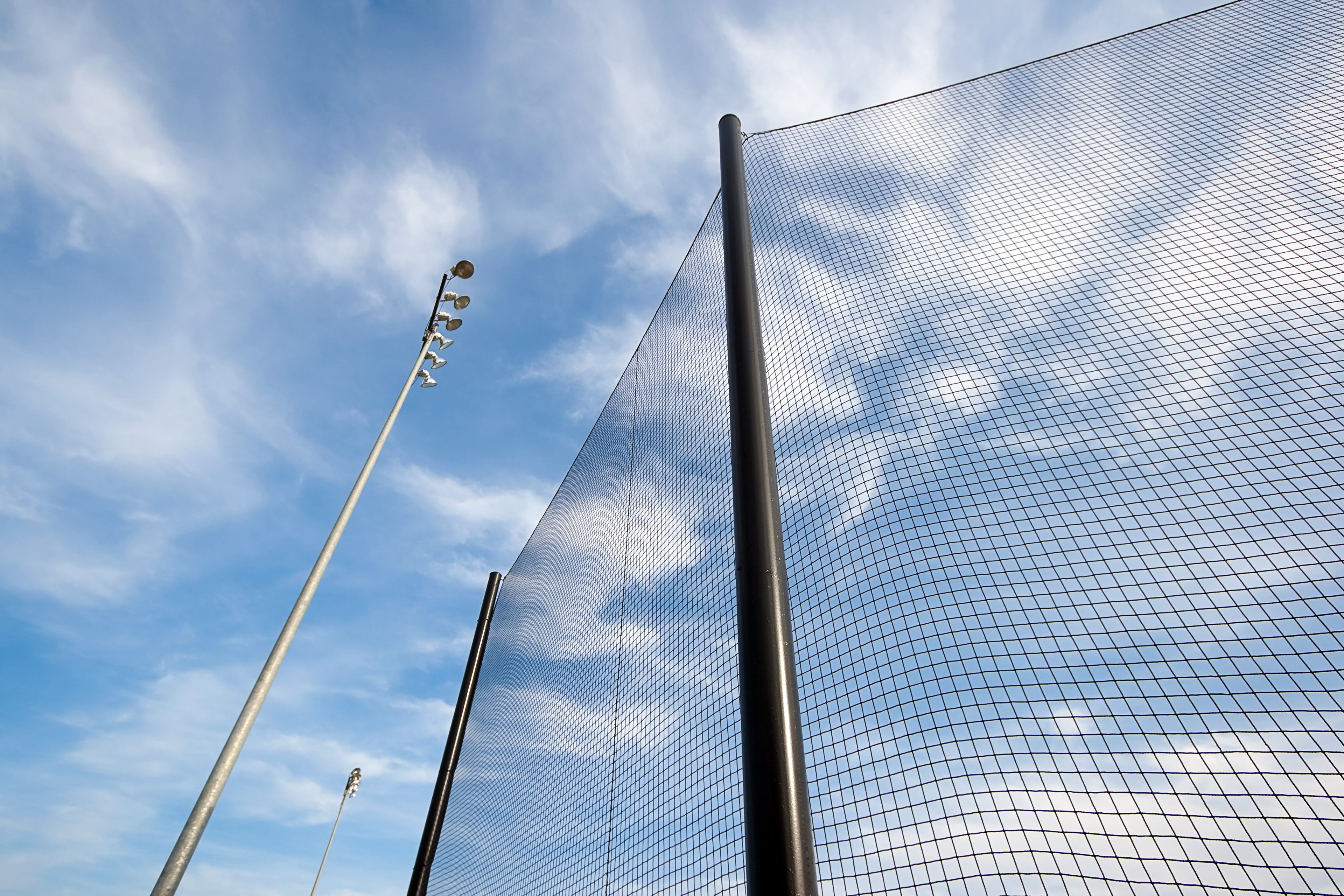 perimeter netting against a blue sky with clouds